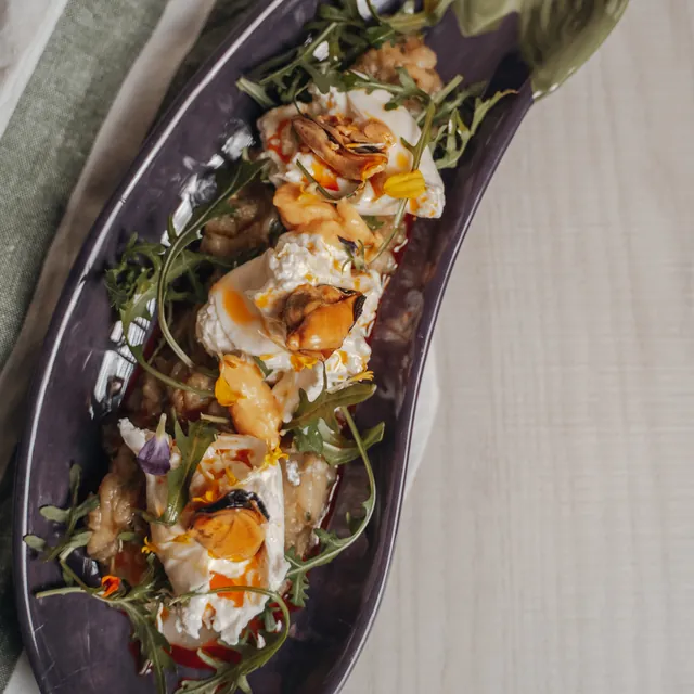 Aubergine with spiced Greek yoghurt, rocket and flowers, on an aubergine-shaped plate