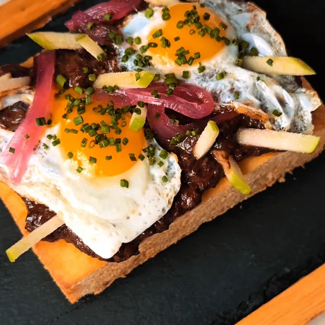 Focaccia with León black pudding, fried quail eggs, apple and pickled onion, on a slate