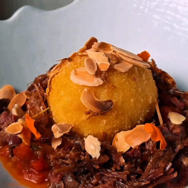 A crispy egg on lamb titaina with flaked almonds, on a white plate