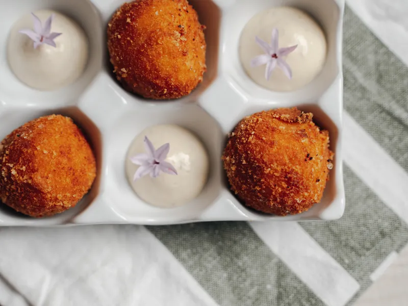 Three croquettes in a white ceramic egg tray, with two creams and lilac flowers, on the striped tea towel