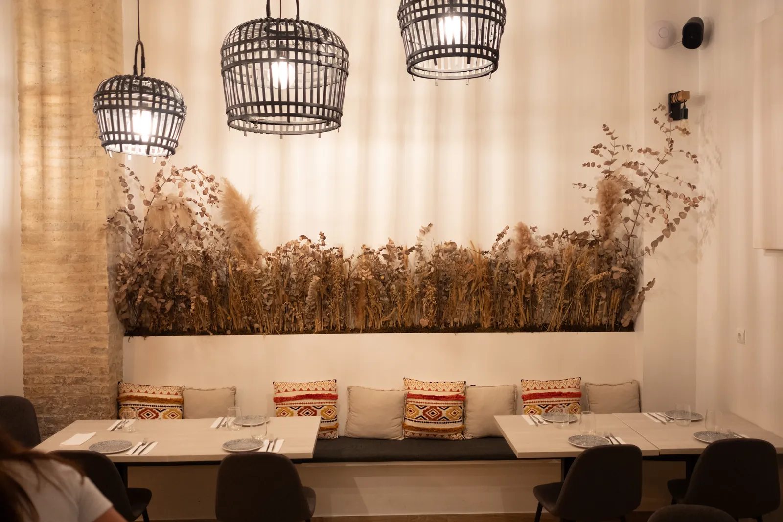 Dining room with a long bench, diamond-patterned cushions, three wicker lamps and dried wheat on the wall