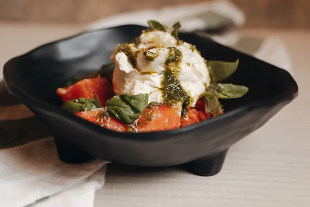 Burrata con tomate y pesto en un cuenco negro