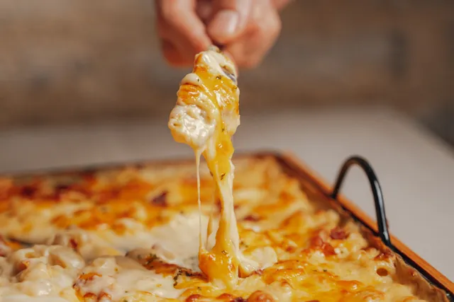 Una mano tira del queso de un mac and cheese recién gratinado en su bandeja