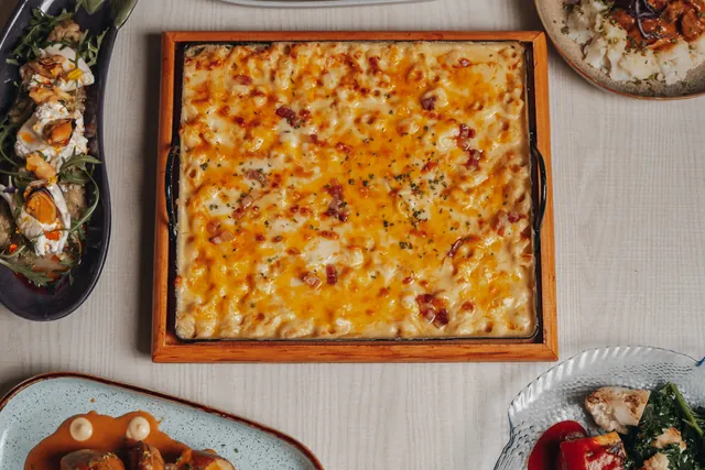 Una mesa vista desde arriba con una bandeja de mac and cheese, berenjena y platos para compartir