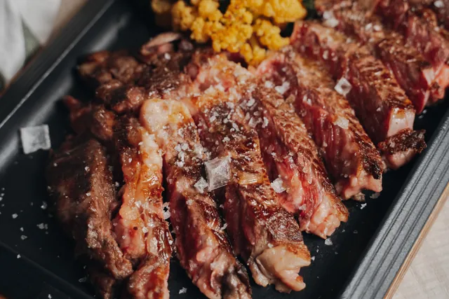Carne de vaca madurada cortada en tiras sobre una plancha negra, con sal en escamas