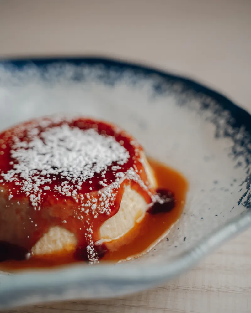 Un flan con caramelo y azúcar glas, en un cuenco blanco con el borde azul