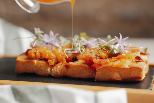 Se vierte una salsa sobre una tosta cubierta de verduras y flores
