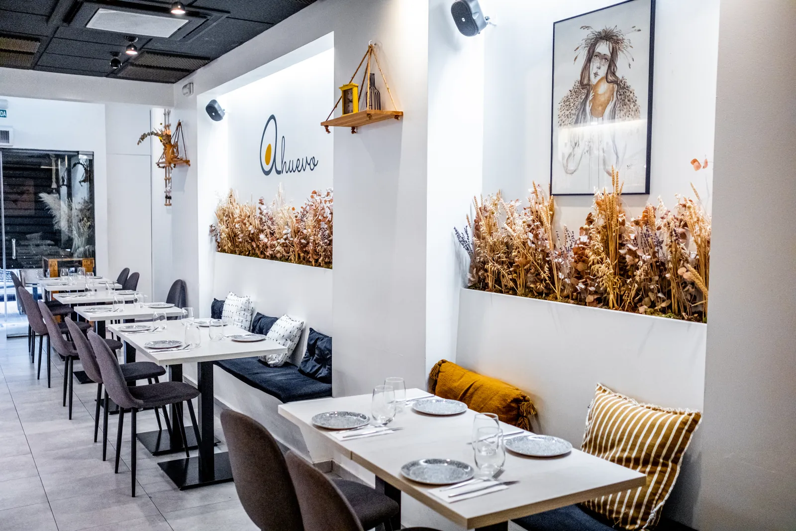The A Huevo dining room: set tables, long benches with cushions, dried wheat on the wall and its logo