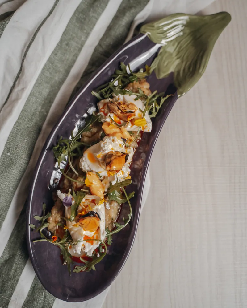 Aubergine with spiced yoghurt, rocket and flowers, on an aubergine-shaped plate