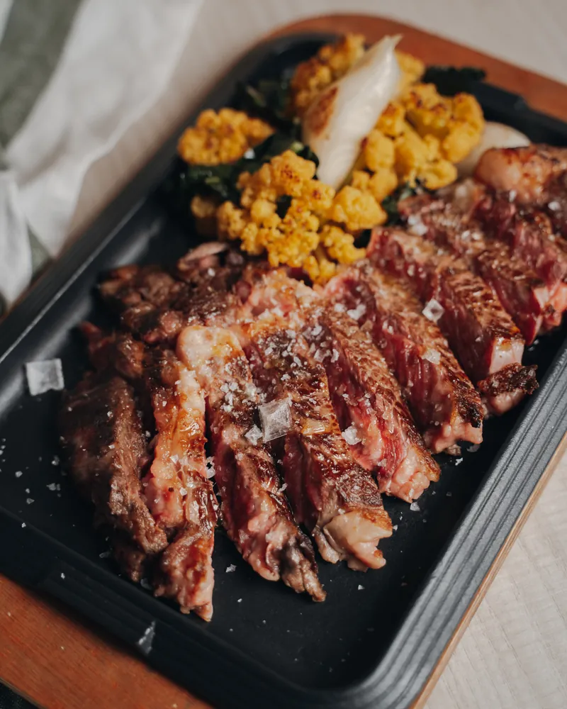 Dry-aged beef chop sliced into strips on a black griddle, with roast cauliflower