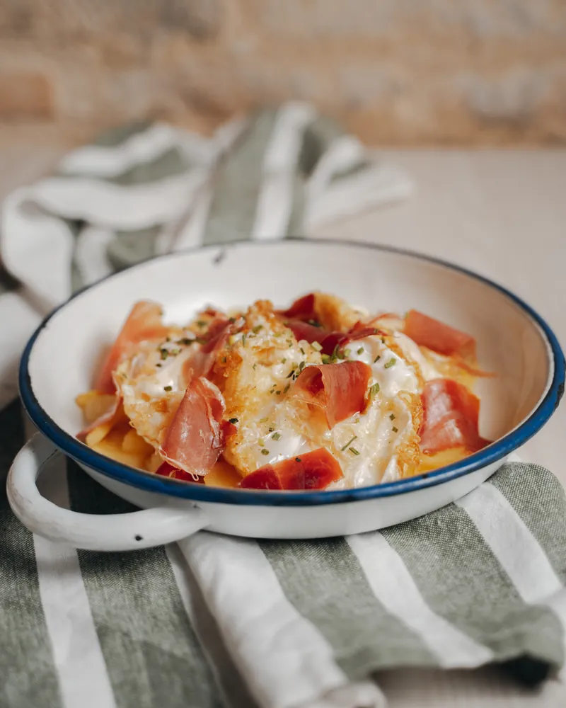 ‘Ahuevos’ rotos with ham in a white enamel pan with a blue rim