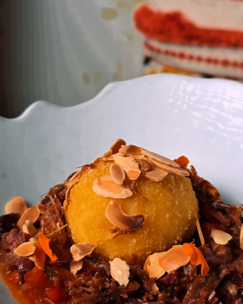 A crispy egg on titaina with flaked almonds, on a white plate