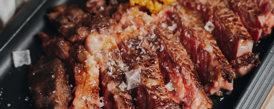 Dry-aged beef chop sliced into strips, on a black griddle